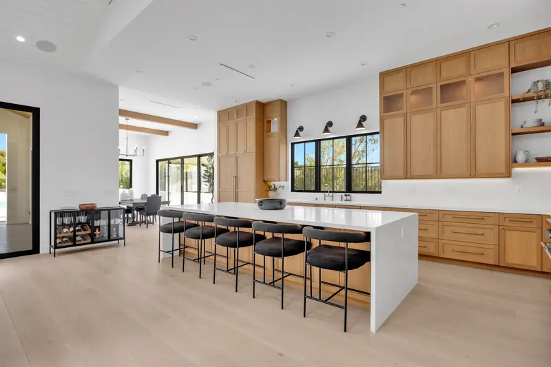 Kitchen countertops in Porter Ranch, CA: open kitchen with a long white island countertop, black counter stools and oak cabinetry