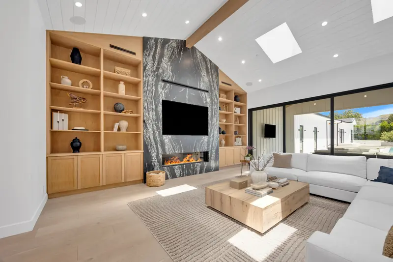 Slab fireplace in Porter Ranch, CA: full-height dark veined slab fireplace wall with a linear fireplace and oak built-ins