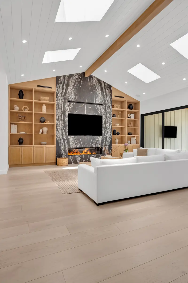 Slab fireplace in Porter Ranch, CA: living room with a full-height dark veined slab fireplace wall between oak bookshelves under a vaulted, skylit ceiling