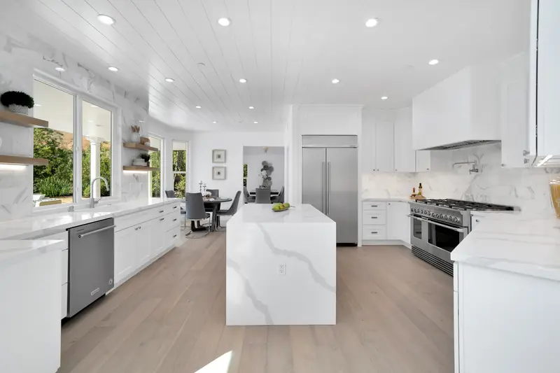Kitchen countertops in Sherman Oaks, CA: white kitchen with a veined white waterfall island at its center and matching perimeter countertops
