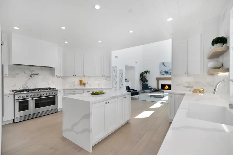 Kitchen countertops in Sherman Oaks, CA: white kitchen with a veined waterfall island, range and slab backsplash