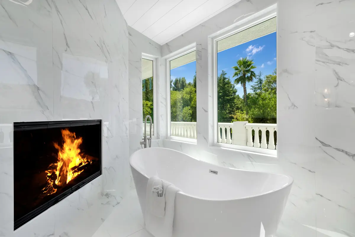 Slab fireplace in Sherman Oaks, CA: white veined slab wall with a built-in fireplace beside a freestanding tub
