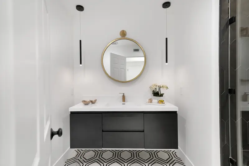 Vanity countertop in Sherman Oaks, CA: floating black vanity with a white countertop and round brass mirror